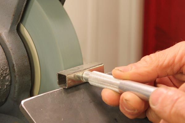 Using a diamond wheel dresser to clean and recreate a flat surface on the aluminum oxide grinding wheel.